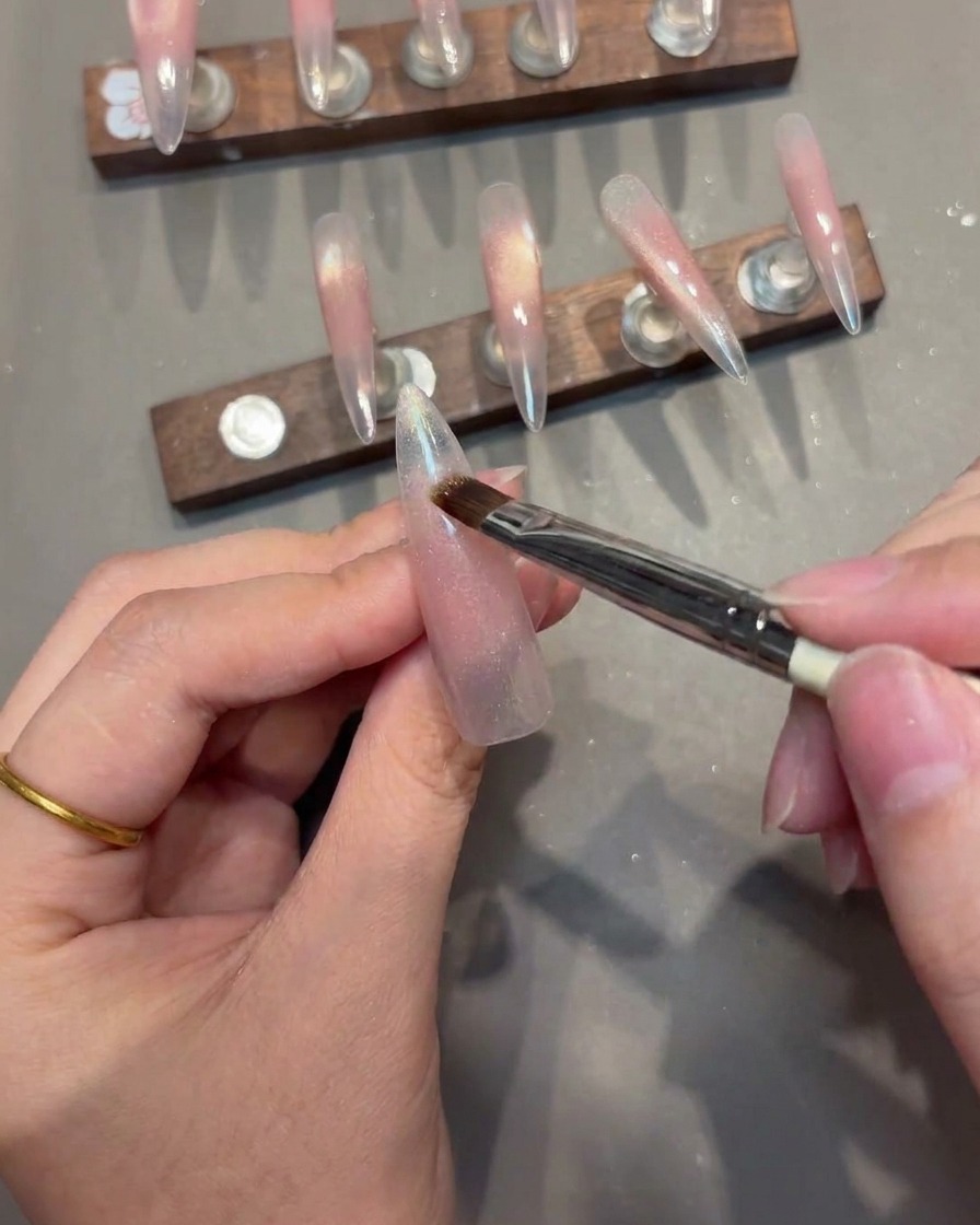 Nahaufnahme eines Nagelpinsels, der Cat-Eye-Gel auf einen Nageltipp aufträgt, während der Magnet für eine scharfe V-Linie positioniert ist.