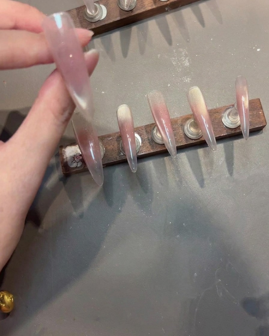 Ein Stamping-Tool drückt ein filigranes, unregelmäßiges weißes Spitzenmuster auf einen Nagel mit rosa Cat-Eye-Gel.