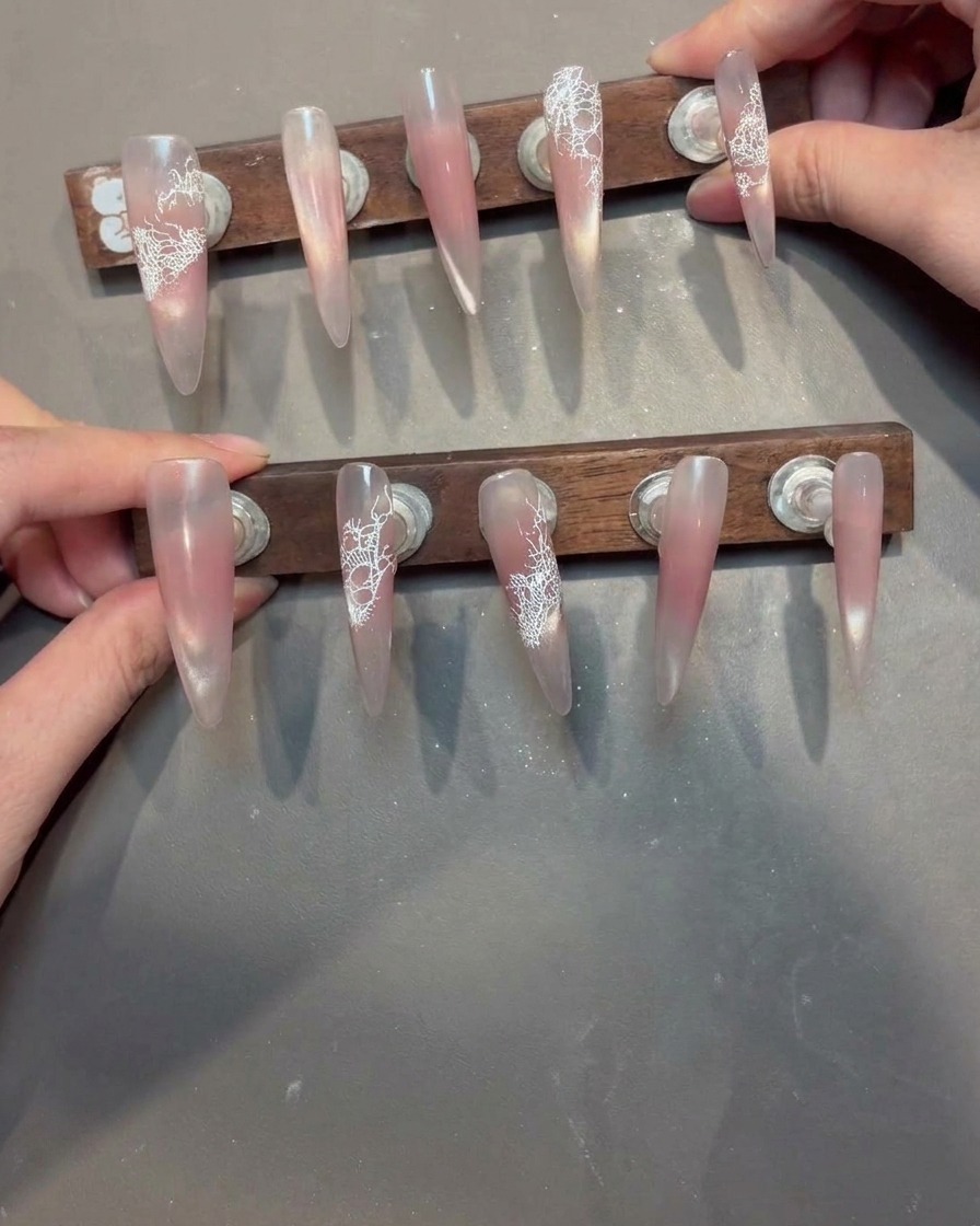 Ein Pinsel trägt klares, viskoses Aufbaugel auf einen Nagel mit weißem Spitzenmuster auf.
