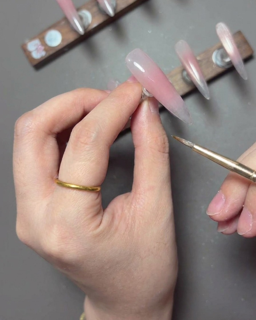 Ein feiner Liner-Pinsel zieht eine dünne, dehnbare Linie aus weißem Spider-Gel über einen manikürten Nagel, um spitzenartige Details zu erzeugen.