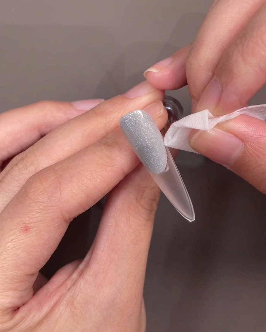 Eine Pinzette zieht eine Silikon-Smile-Line-Schablone ab und enthüllt eine saubere, geschwungene Kante auf dem blauen Gel.