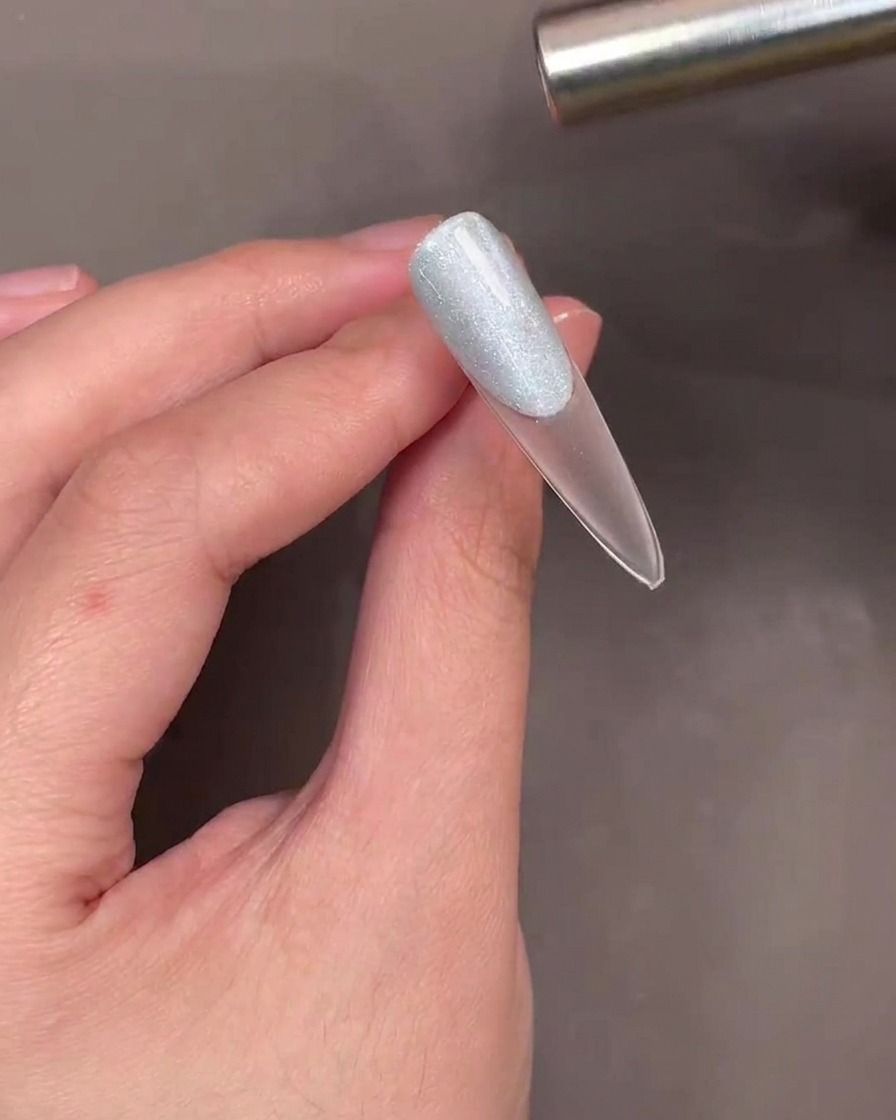 Ein Magnetstab wird über einen mit blauem Cat-Eye-Gel überzogenen Nagel gehalten, um einen Schimmereffekt zu erzeugen.