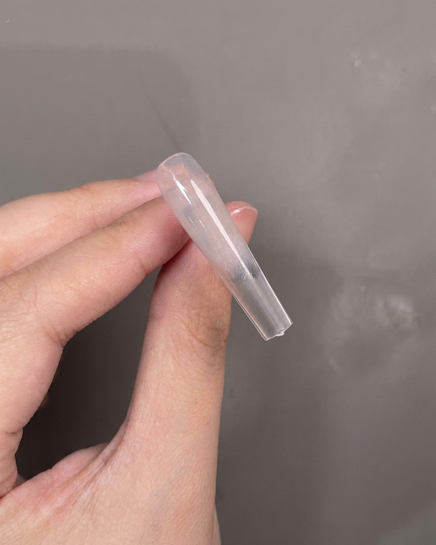 Ein blaues Silikonwerkzeug trägt weißes Strukturgel waagerecht über die Mitte eines Nageltips auf.
