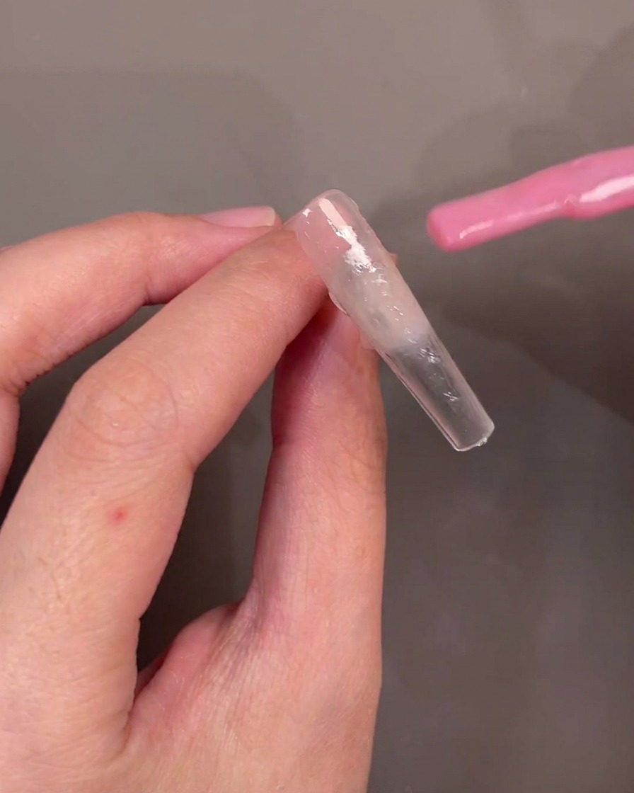 Ein Pinsel streicht transparentes rosa Gel diagonal über einen Nageltip.