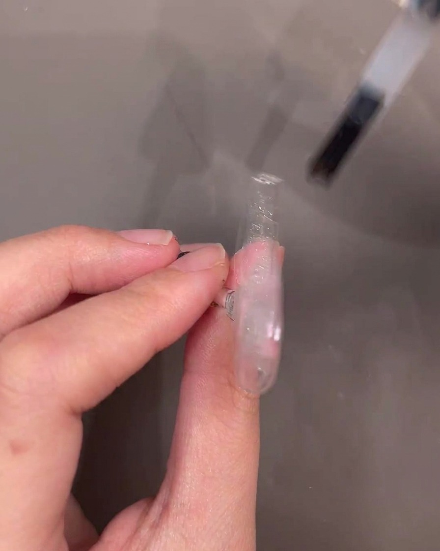 Ein Gelpinsel trägt eine Schicht klares Aufbaugel über den verzierten Nagel auf.