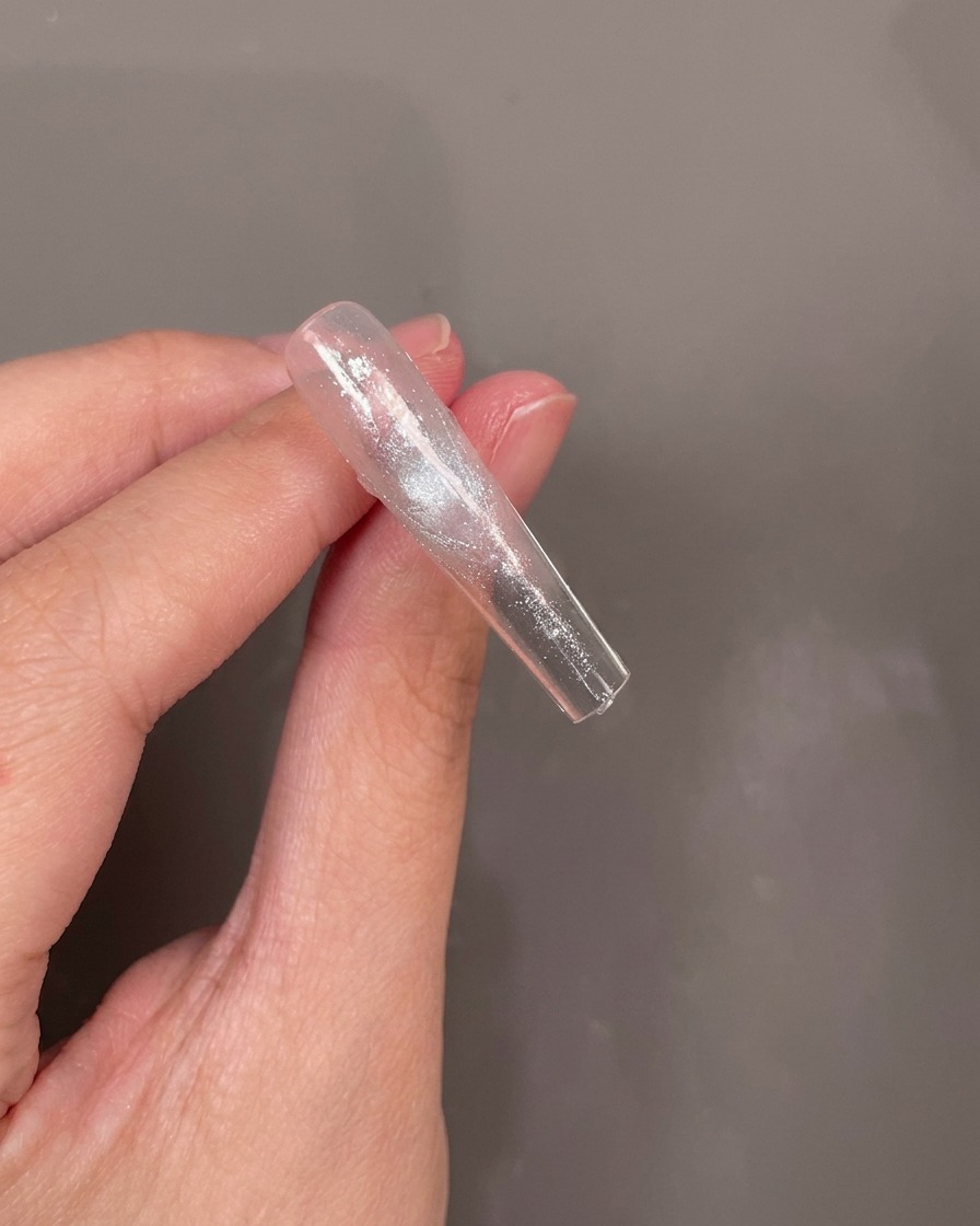 Die Unterseite eines Nageltips, auf die eine kleine blaue Trockenblume in eine nasse Gelschicht gelegt wird.