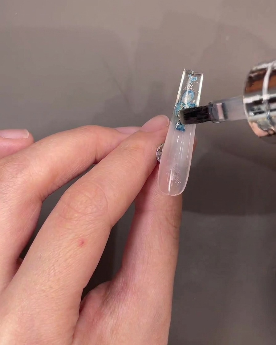 Ein Pinsel trägt eine Schicht Top Coat über die Trockenblumen auf der Unterseite auf.
