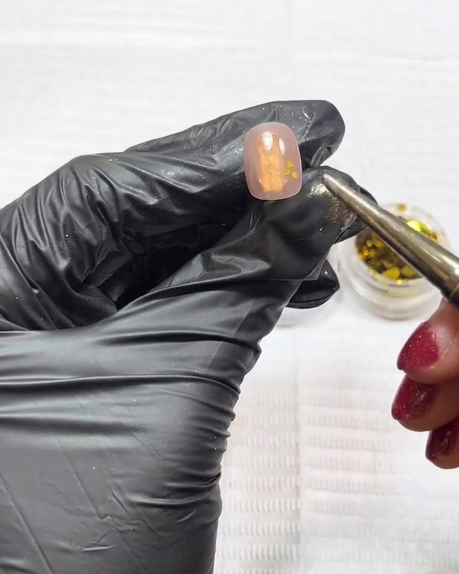 Ein Dotting-Tool platziert feine Gold- und Silber-Pailletten punktuell auf der klebrigen Gelschicht.