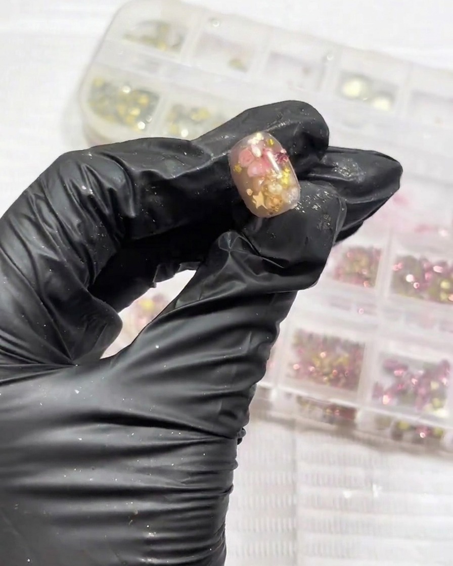 Kleine, funkelnde Strasssteine werden präzise im Nagelbettbereich platziert.