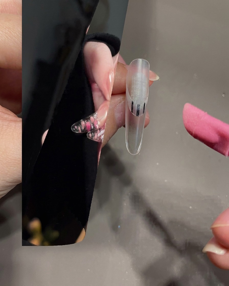 Ein Nail-Art-Pinsel verteilt weißes Gel auf der Spitze eines transparenten Nagels.
