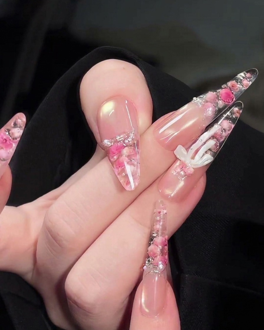 Ein Präzisionspinsel platziert winzige weiße Perlen und Strasssteine auf dem floralen Design auf der Rückseite des Nagels.