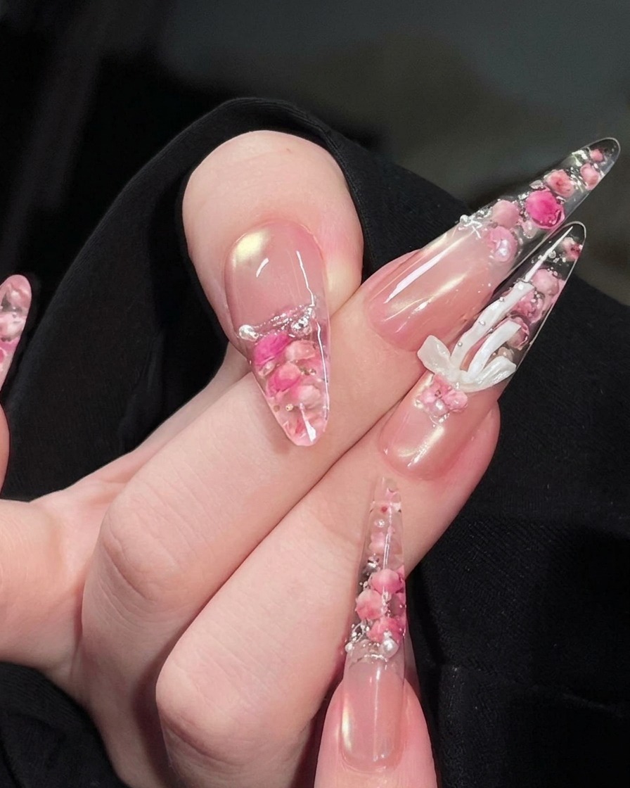 Eine Hand unter einer UV-Nagellampe, die eingekapselten Rosen- und Perlendesigns auf den Nägeln sind sichtbar.