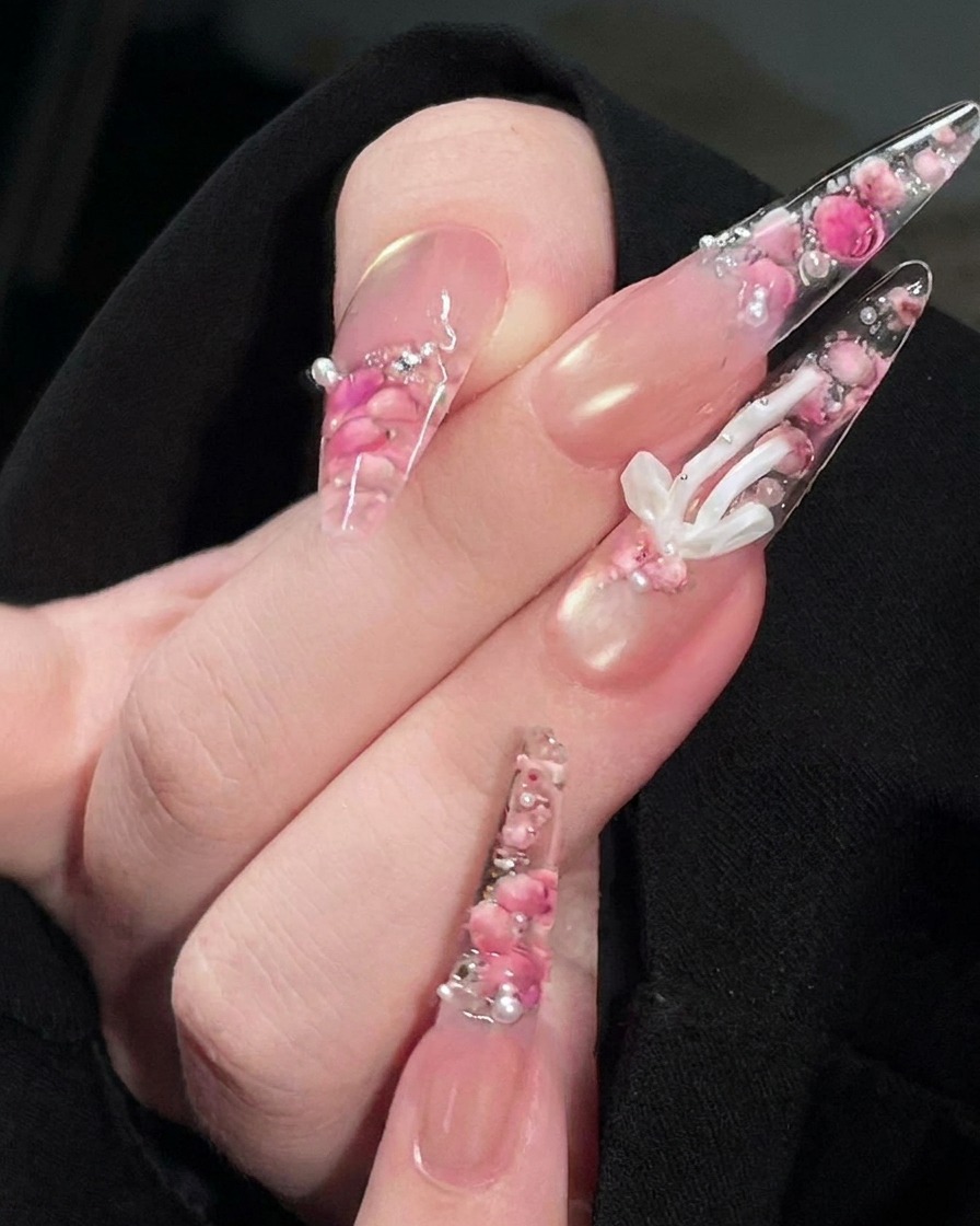 Ein Pinsel trägt einen klaren, glänzenden Top Coat auf die Oberfläche des fertigen Rosen-Nageldesigns auf.