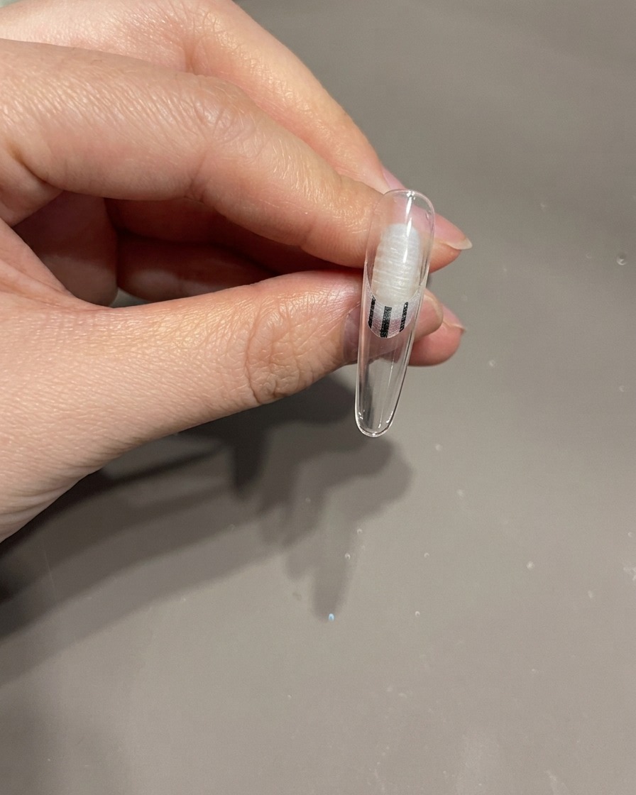 Nahaufnahme einer Hand, die einen Fingernagel mit einer 3D-Schleife zum Aushärten unter eine UV-Nagellampe legt.