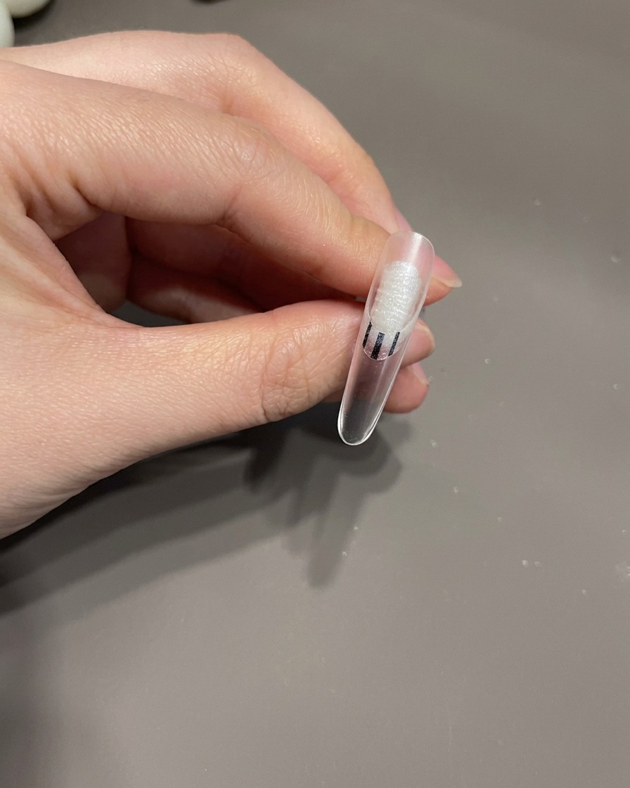 Ein Detailpinsel zeichnet dünne weiße Linien in einem Wirbelmuster über einen gelackten Fingernagel.