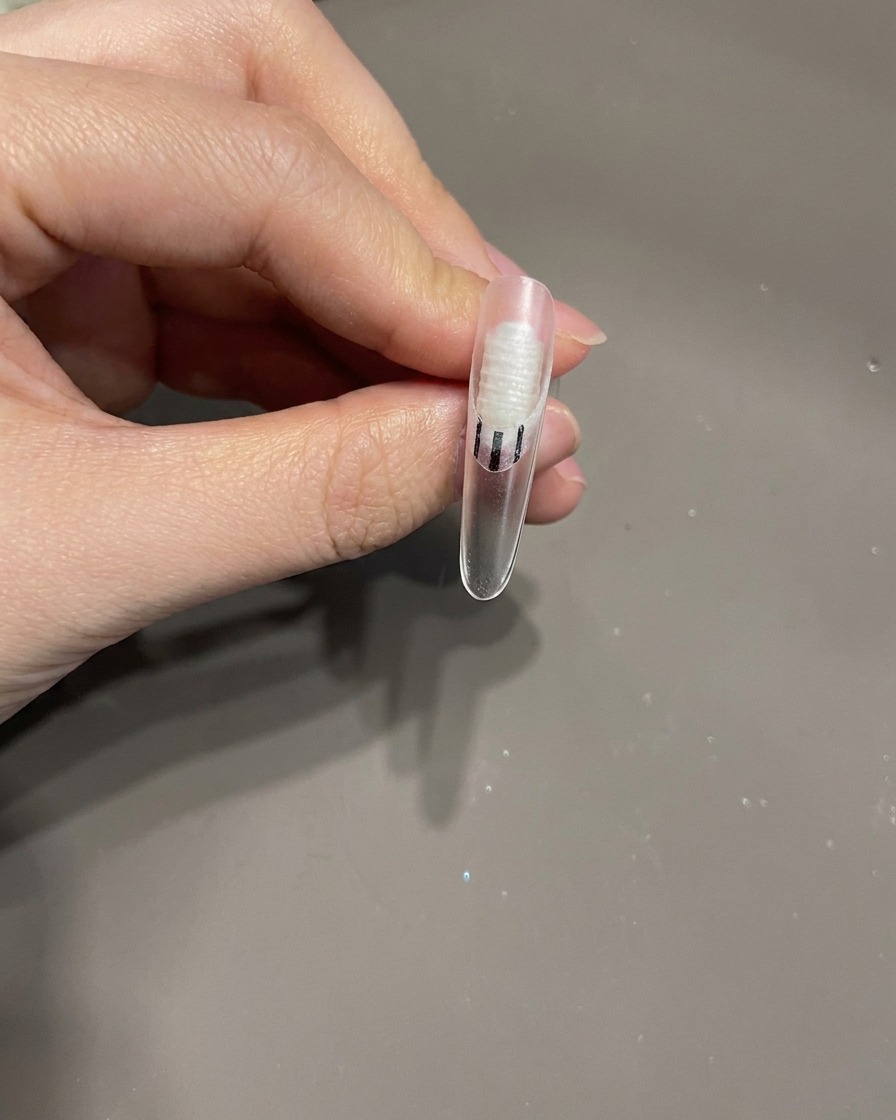 Ein Nagelpinsel gibt einen kleinen Tropfen klaren Top Coat als Kleber für eine Verzierung auf eine Nageloberfläche.