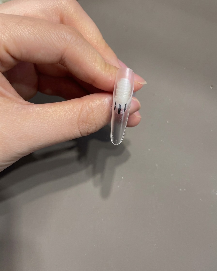 Eine Pinzette platziert eine kleine 3D-Gelschleife auf der Oberfläche eines manikürten Fingernagels.