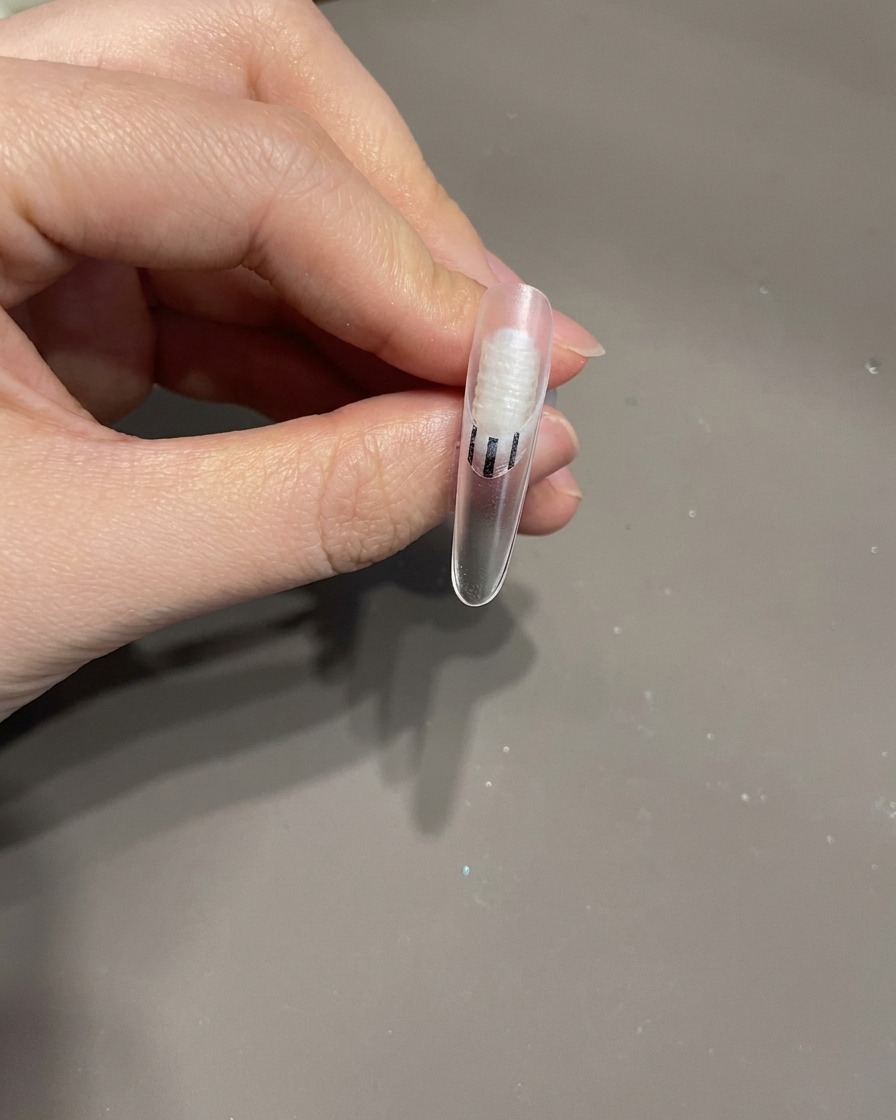 Ein fertiger Fingernagel mit einer 3D-Schleife und weißen Schnörkellinien in einer UV-Lampe für den letzten Aushärtungsprozess.