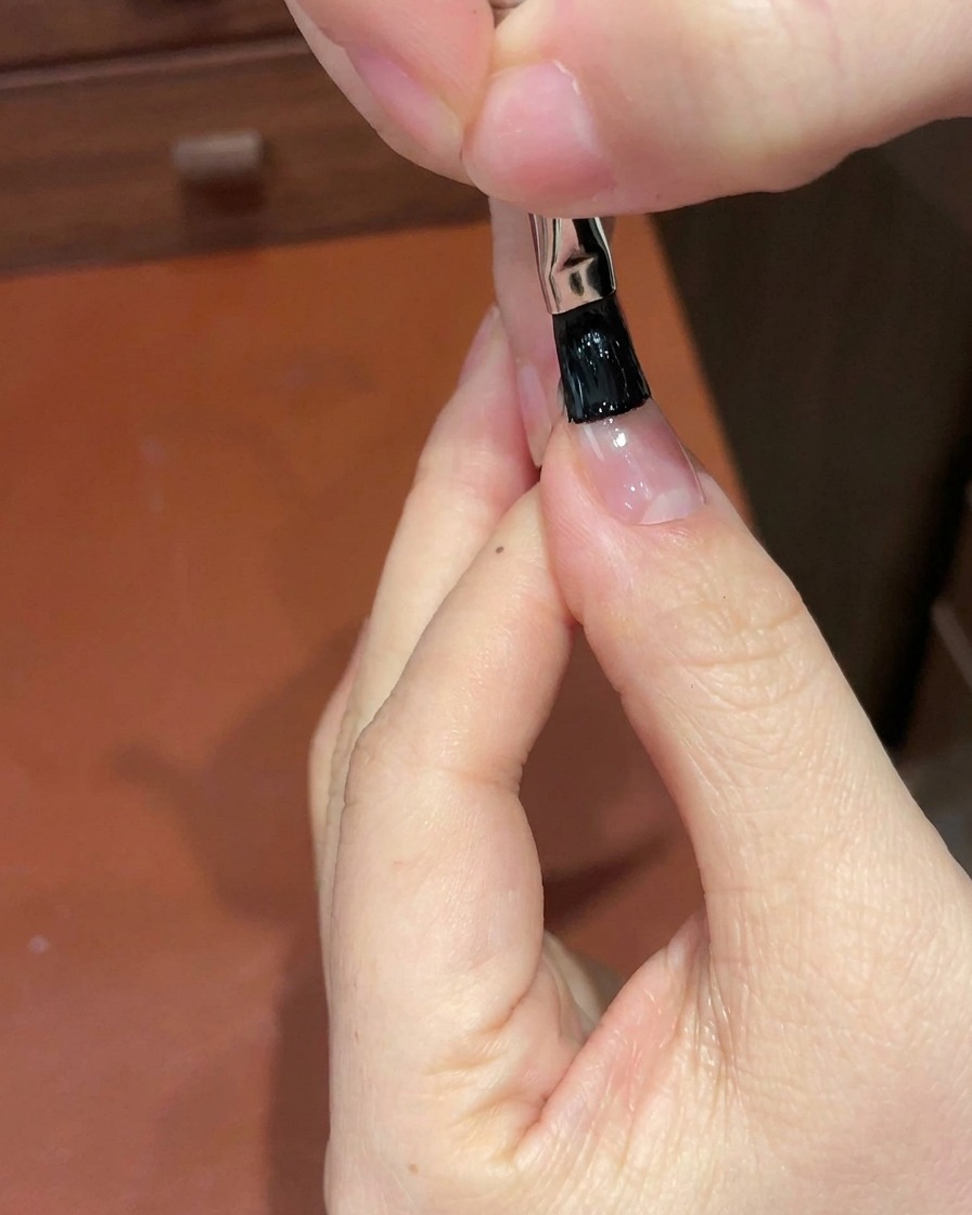 Detailansicht eines Pinsels, der schwarzes Gel auf die Nagelspitze aufträgt.