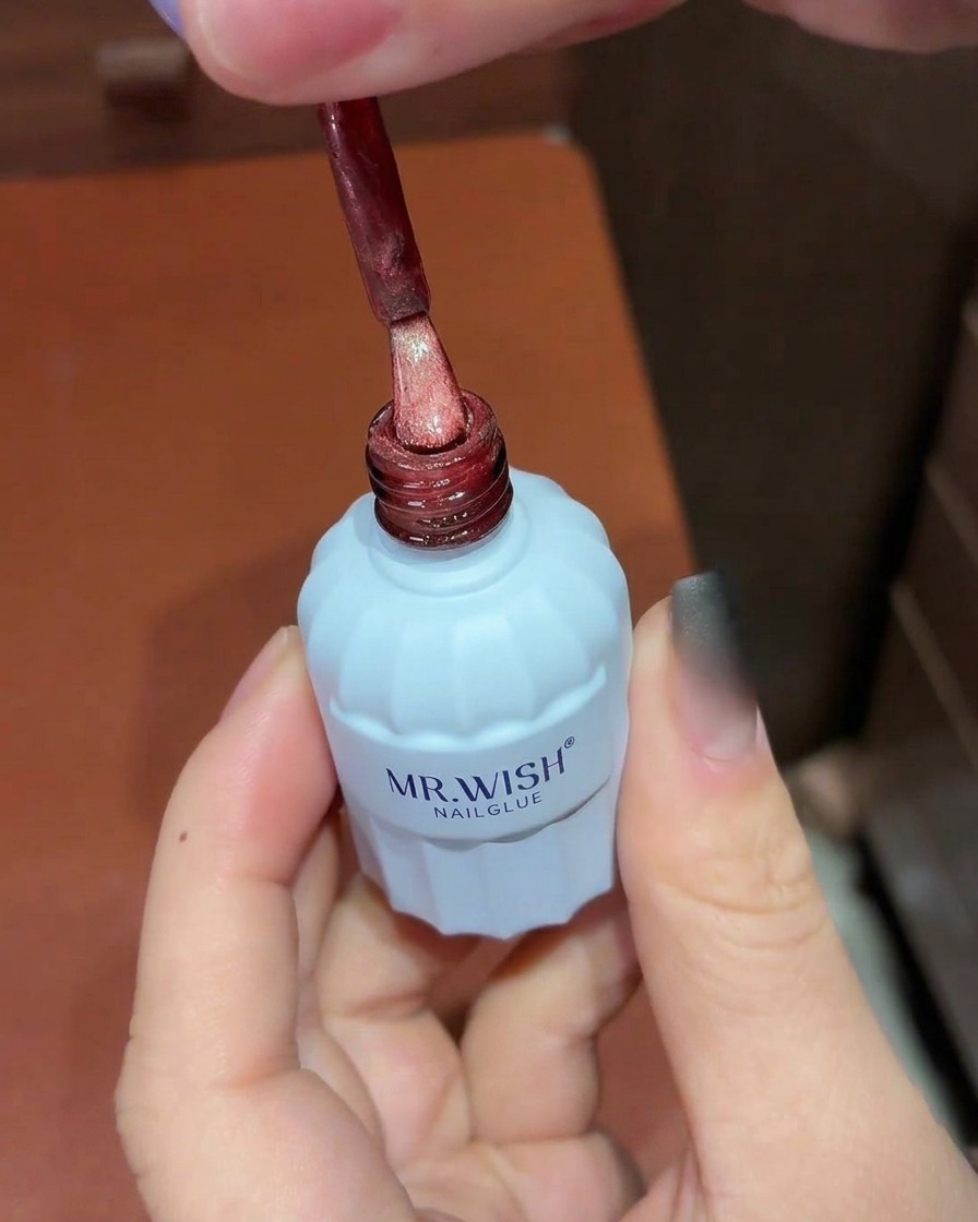 Ein Pinsel trägt schimmerndes rotes Cat-Eye-Gel über den schwarzen Ombré-Nagel auf.