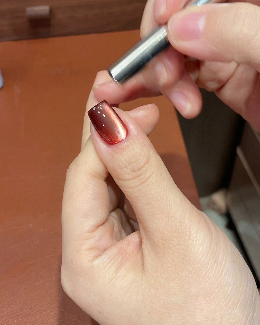 Ein Magnettool wird in die Nähe des Nagels gehalten, um die Schimmerpartikel im roten Gel zu bewegen.