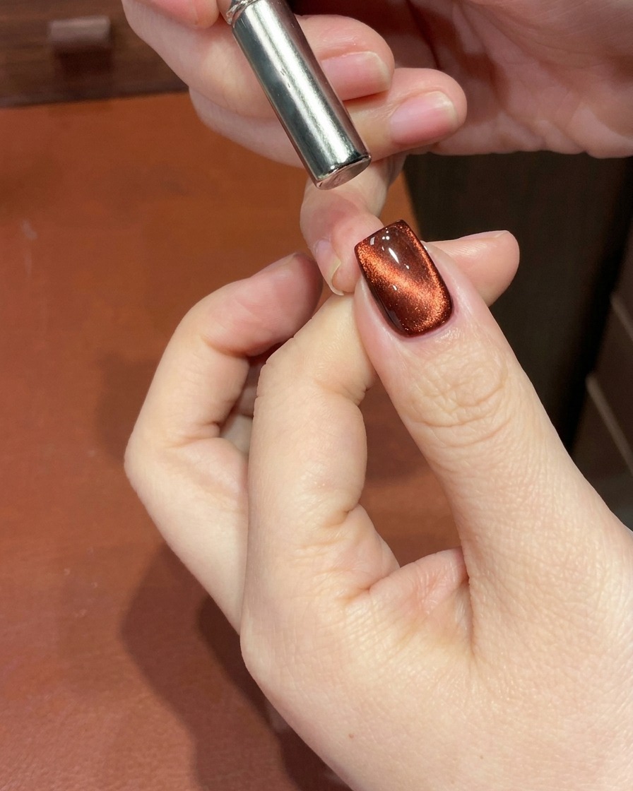 Nahaufnahme eines roten Cat-Eye-Gelnagels mit einem Magneten am Nagelbett, der den Schimmer als Verlauf formt.