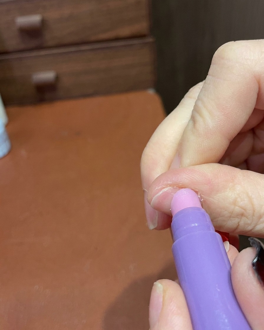Die Spitze eines Pflege-Stiftes glättet sanft die Oberfläche und Kanten des fertig manikürten Nagels.