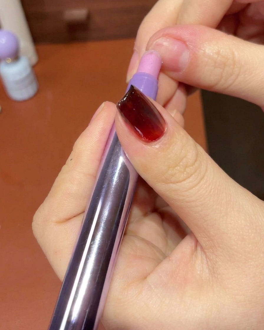 Eine Hand wischt mit einem fusselfreien Tuch über die Haut und Ränder des fertig manikürten Nagels.