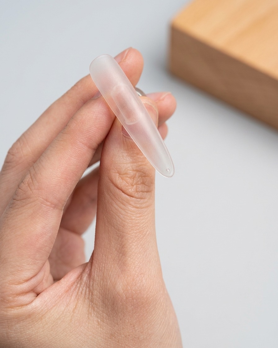 Ein Pinsel trägt eine Schicht schimmerndes Cat-Eye-Gel auf die obere Hälfte eines klaren Nagel-Tips auf.