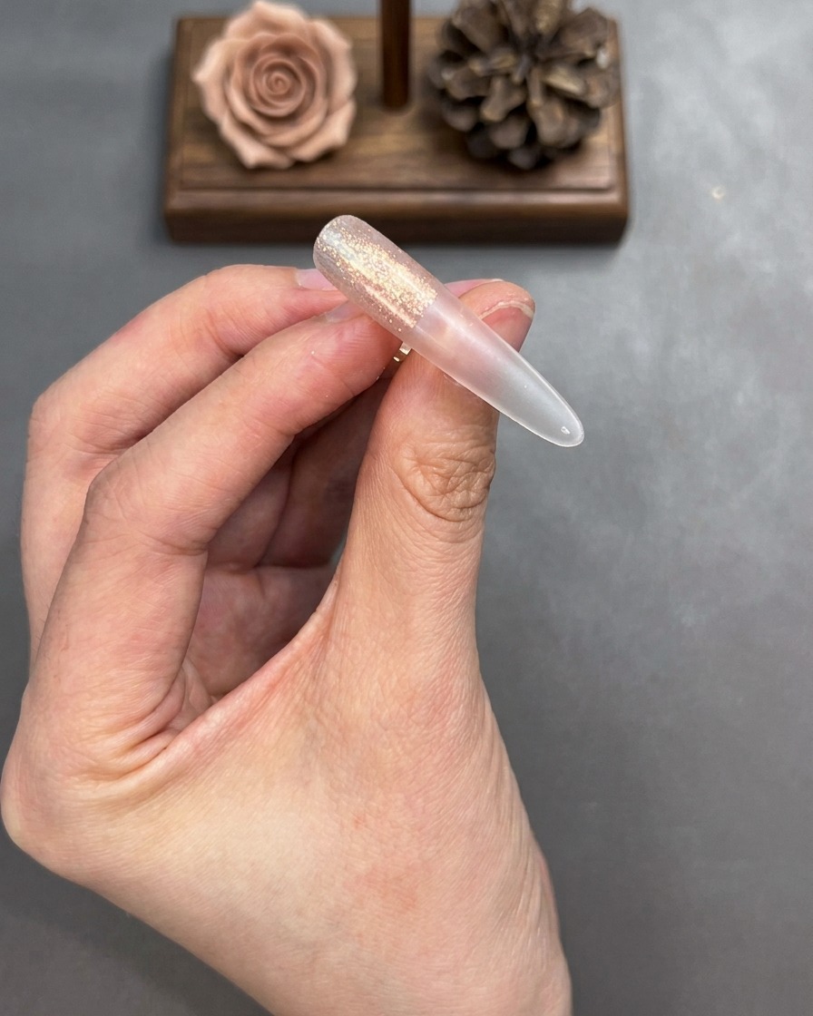 Ein Pinsel verblendet die Ränder des aufgetragenen Cat-Eye-Gels auf einem Nagel-Tip für einen weichen Übergang.