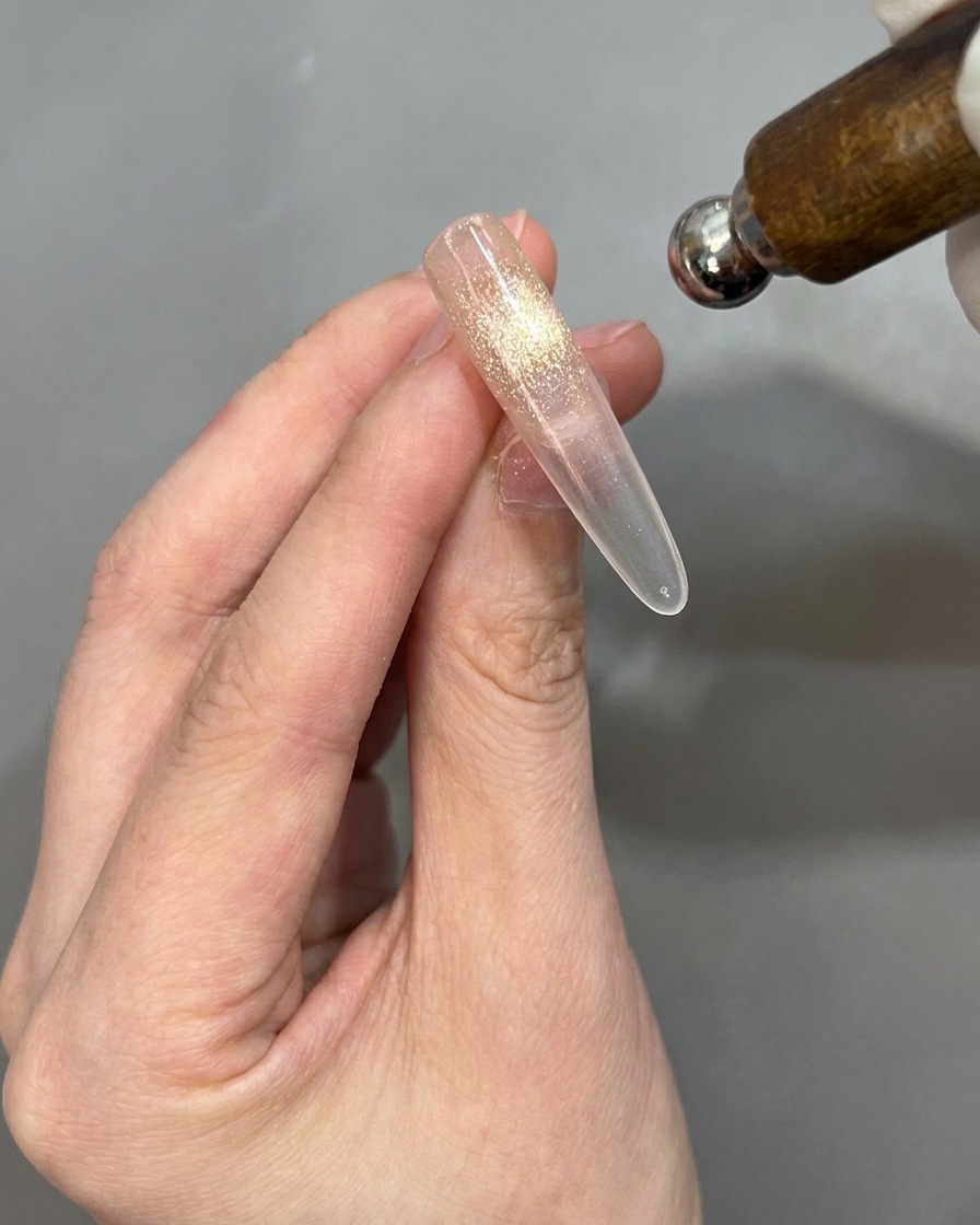 Ein Magnet wird nahe an einen Nagel-Tip gehalten, um den Cat-Eye-Effekt zu aktivieren.