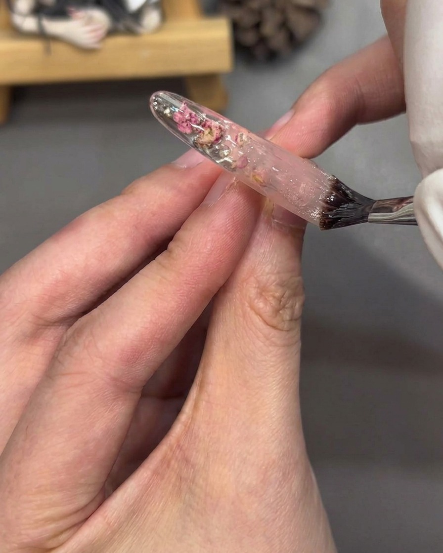 Ein Pinsel trägt glänzenden Top-Coat auf den vollständig verzierten Nagel-Tip auf.