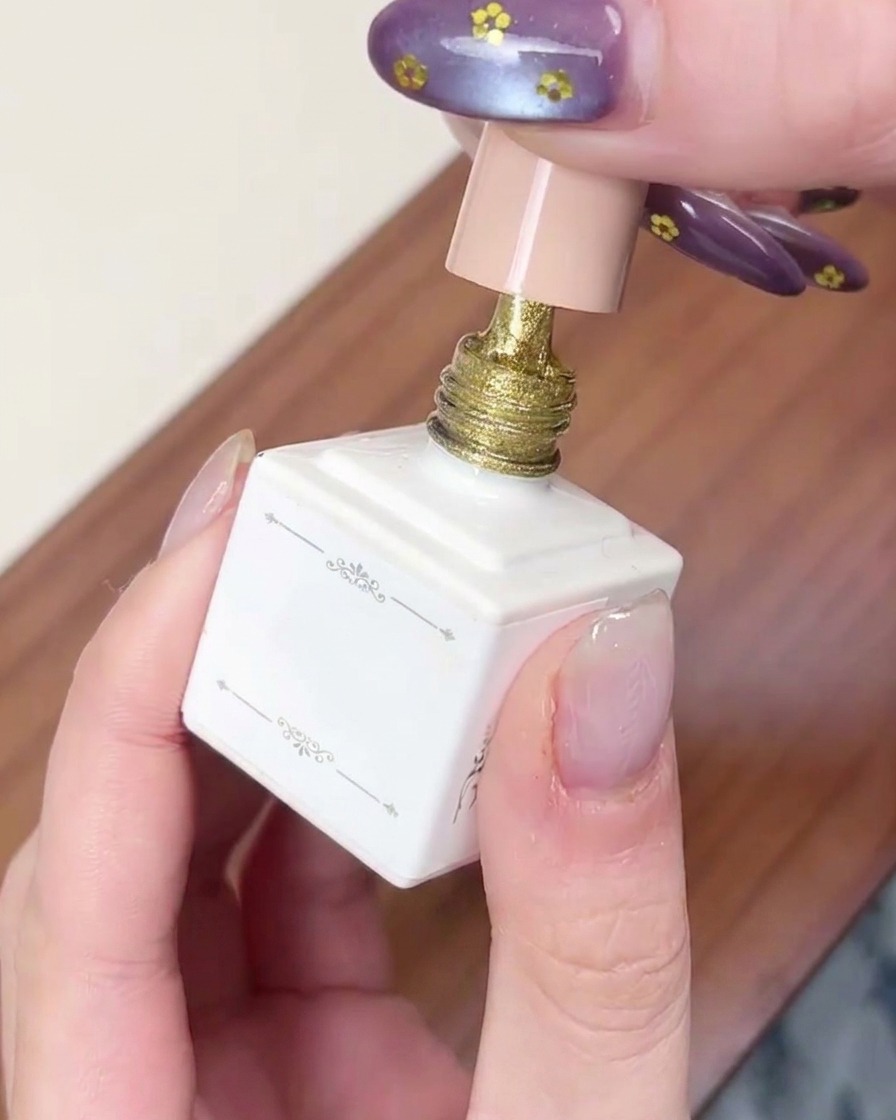 Ein Pinsel trägt eine Schicht schimmerndes goldenes Cat-Eye-Gel auf einen Fingernagel auf.