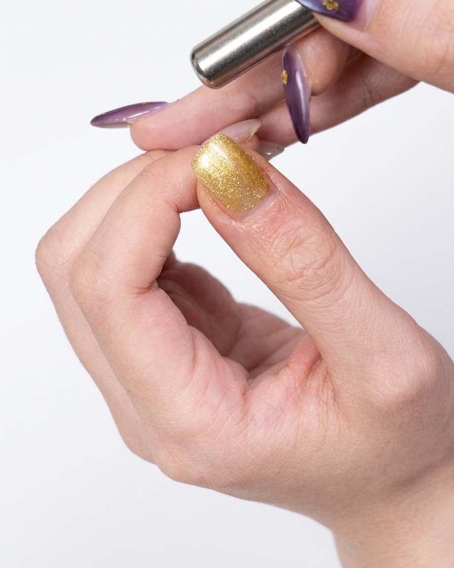 Ein Magnetwerkzeug wird seitlich an den mit Gold-Gel beschichteten Nagel gehalten, um die magnetischen Partikel zu verschieben.