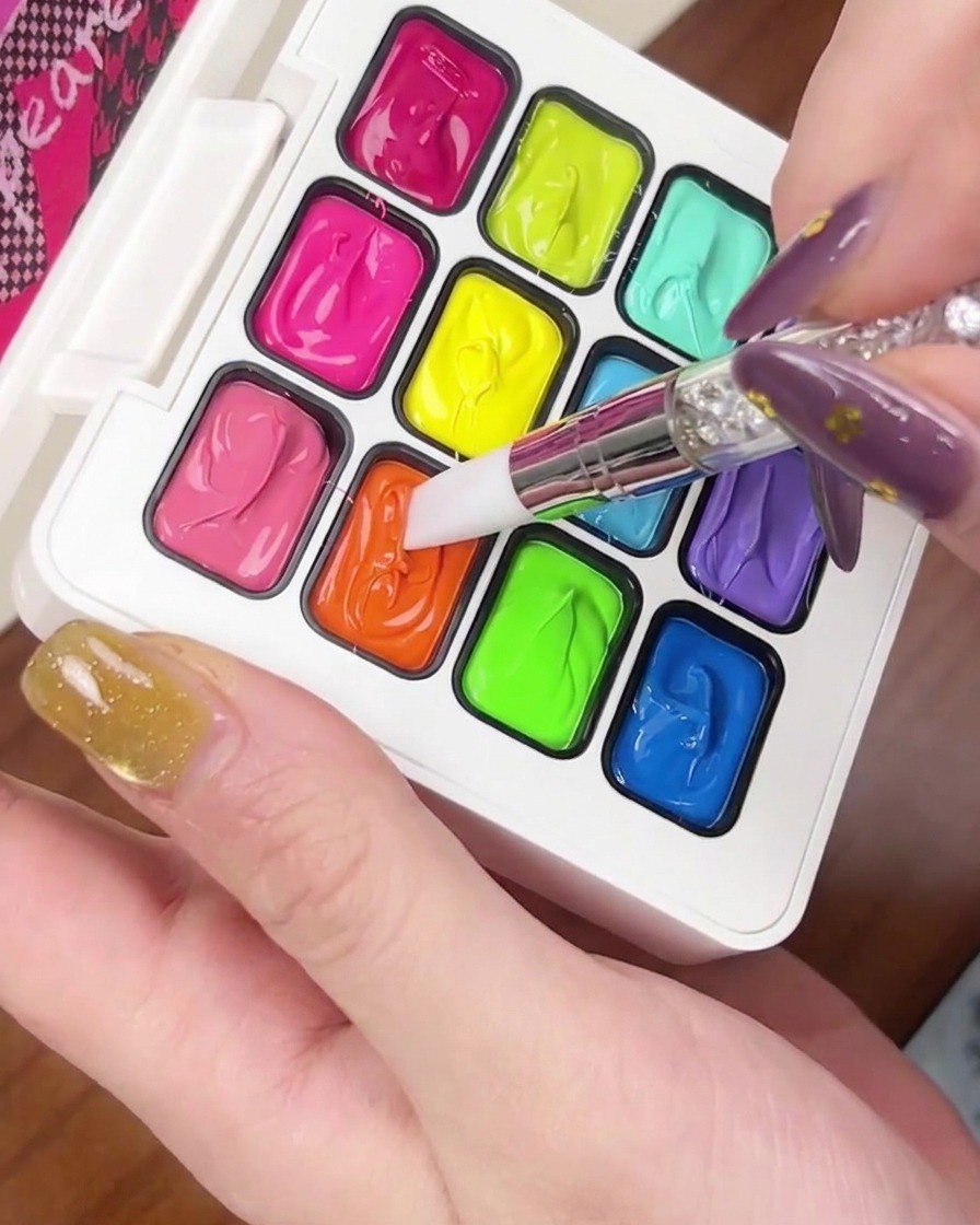 Ein kleiner Klecks orangefarbenes Gel wird auf die Spitze eines goldenen Cat-Eye-Nagels aufgetragen.