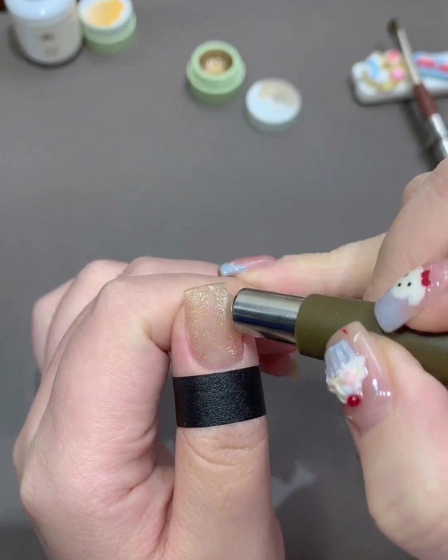 Ein zylindrischer Magnet wird um die Kanten eines Nagels bewegt, der mit glitzerndem, hellgoldenen Cat-Eye-Gel lackiert ist.
