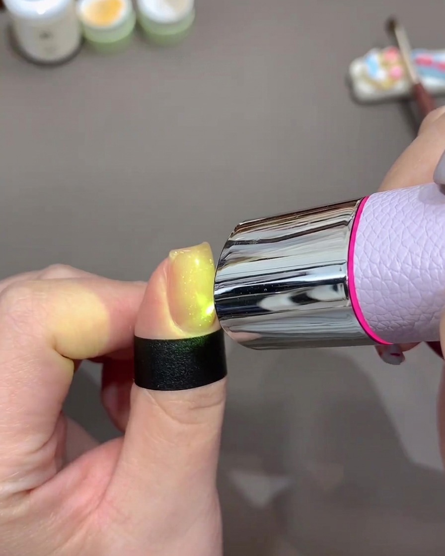 Ein Fingernagel leuchtet hell unter einer kleinen, tragbaren UV/LED-Lampe beim Aushärten des Gels.
