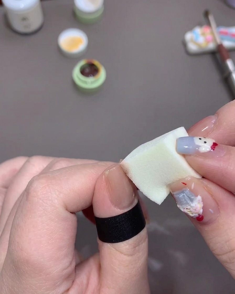 Eine Hand tupft ein geladenes Make-up-Schwämmchen auf die Spitze eines Daumennagels, um einen sanften Farbverlauf zu erzielen.