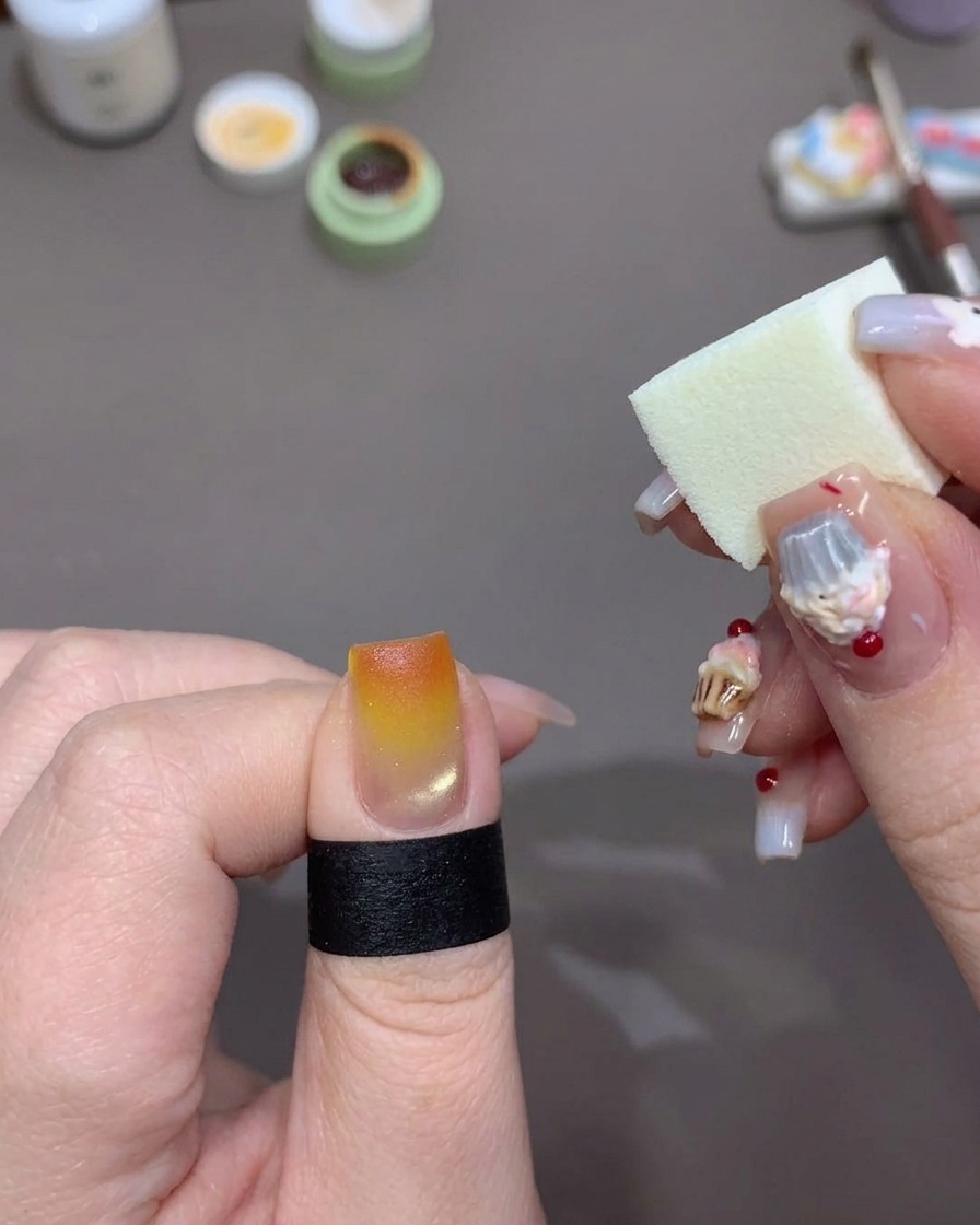 Ein weißer Make-up-Schwamm tupft helles Orange-Gel auf die Spitze eines Fingernagels, um den Sunset-Effekt zu verstärken.
