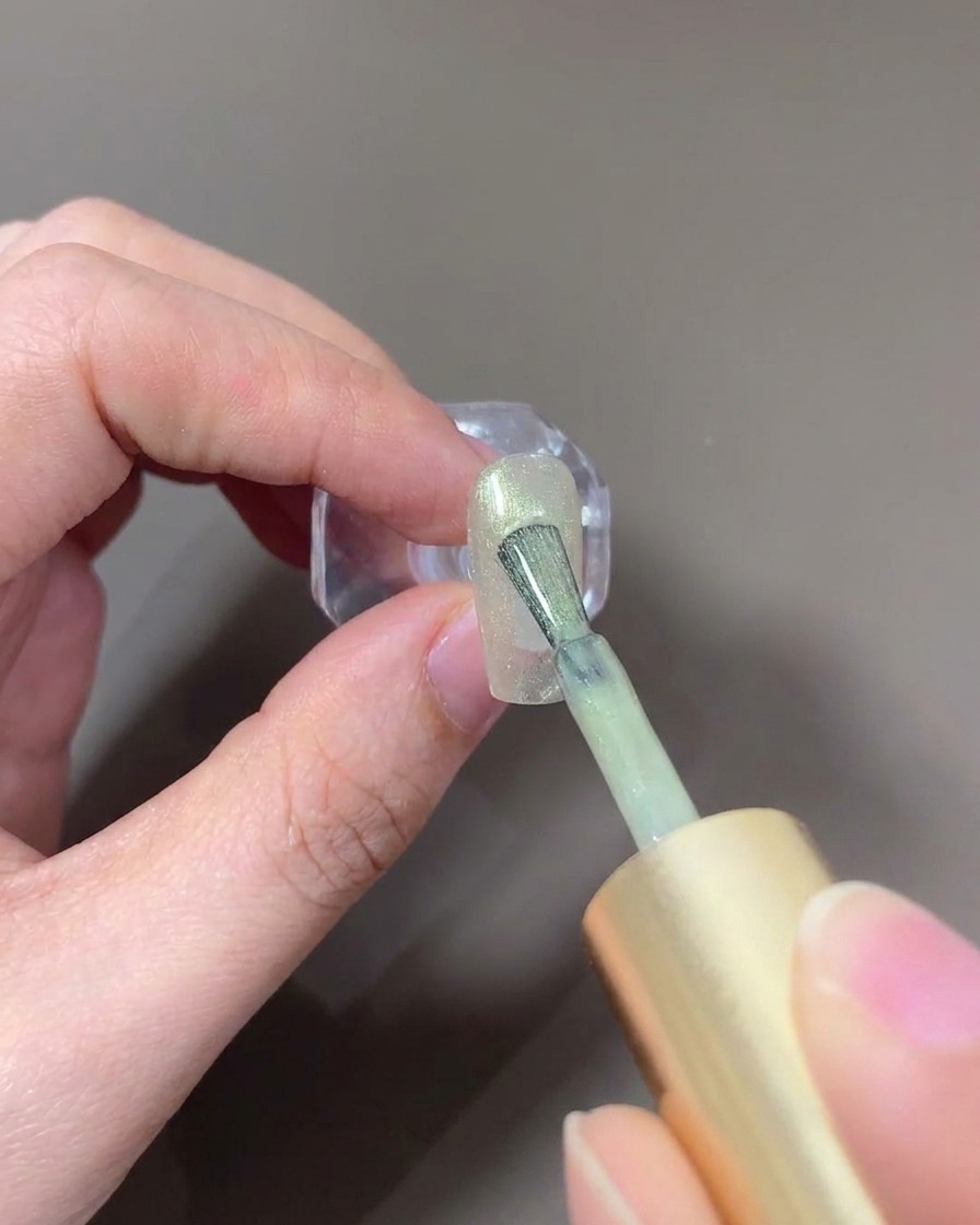 Ein Nagelpinsel beim Auftragen von hellem, gläsernem Cat-Eye-Gel auf den Nagel.