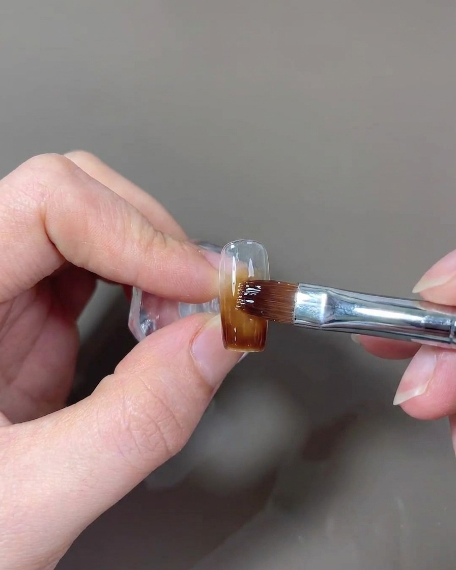 Ein Pinsel beim Auftragen eines glänzenden Top Coats auf den Nagel.