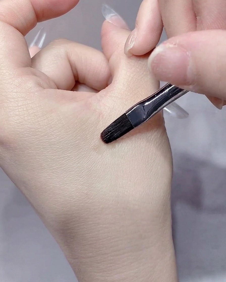 Ein feiner Liner-Pinsel glättet sorgfältig die Ränder des Aufbaugels im Nagelhautbereich.
