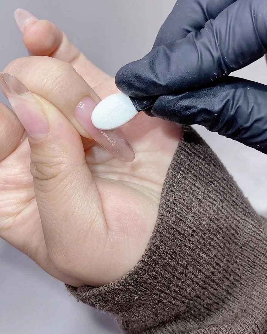 Ein Silikon-Applikator reibt schimmerndes, irisierendes Aurora-Puder auf die Oberfläche eines Nagels.