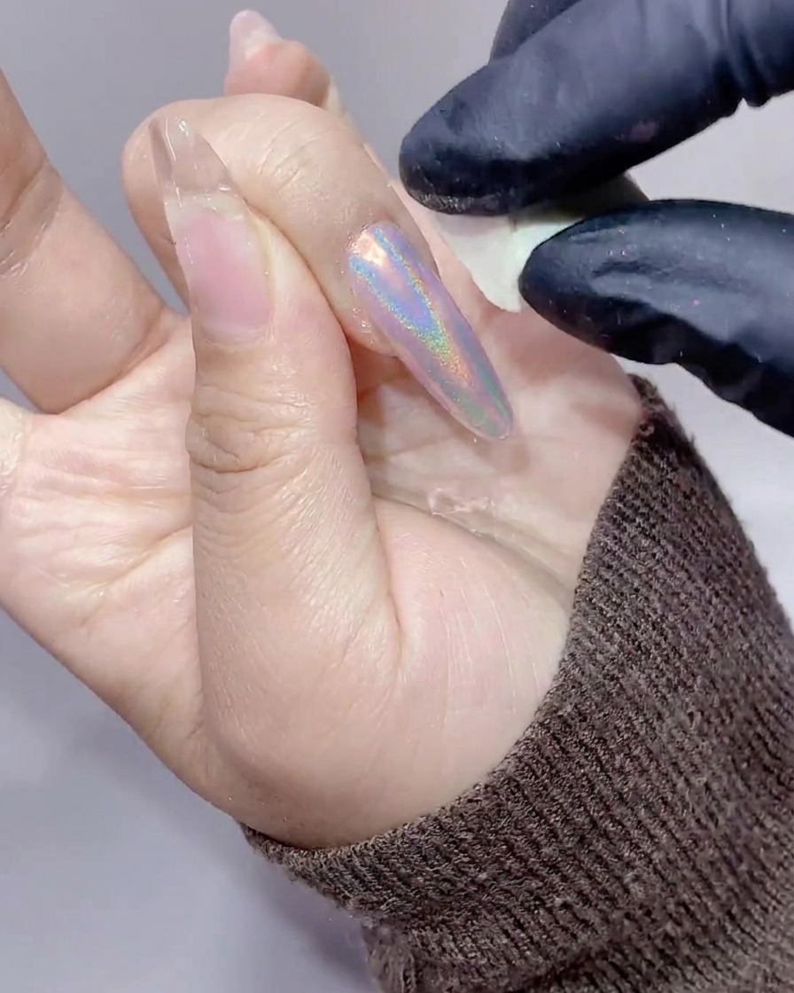 Nahaufnahme eines langen Nagels, der mit einem kleinen weißen Make-up-Schwamm von überschüssigem Aurora-Puder befreit wird.