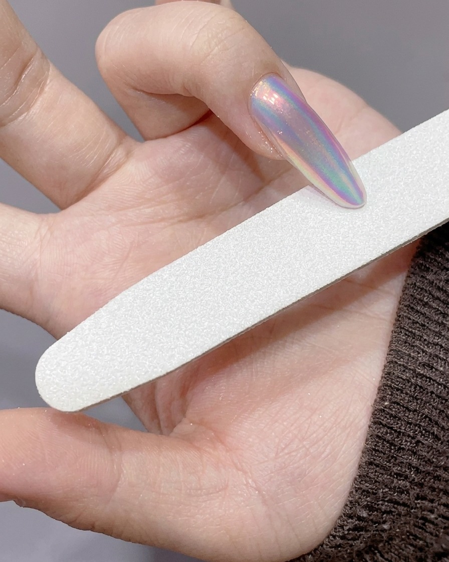 Eine Nagelfeile wird verwendet, um die Kante eines langen, mit Chrom-Puder bestäubten Nagels zu verfeinern.