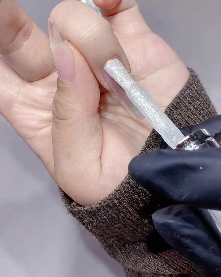 Ein Pinsel trägt eine Schicht glitzerndes, silbernes Diamant-Gel auf einen Nagel auf.
