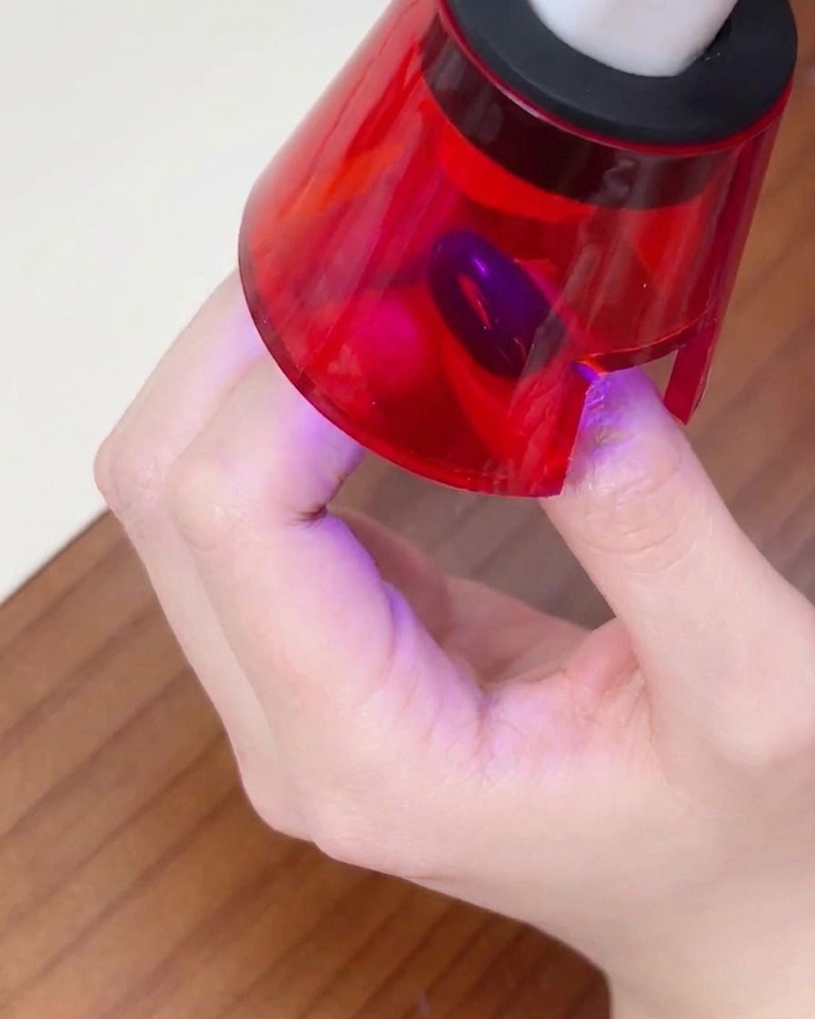 Eine Hand liegt in einer kleinen UV-Nagellampe, der Finger ist zentriert, um den Lack auszuhärten.