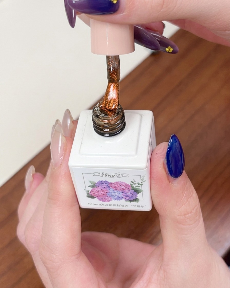 Ein Pinsel trägt eine Schicht durchscheinendes, bernsteinfarbenes, magnetisches Cat-Eye-Gel über der dunkelblauen Basis auf.