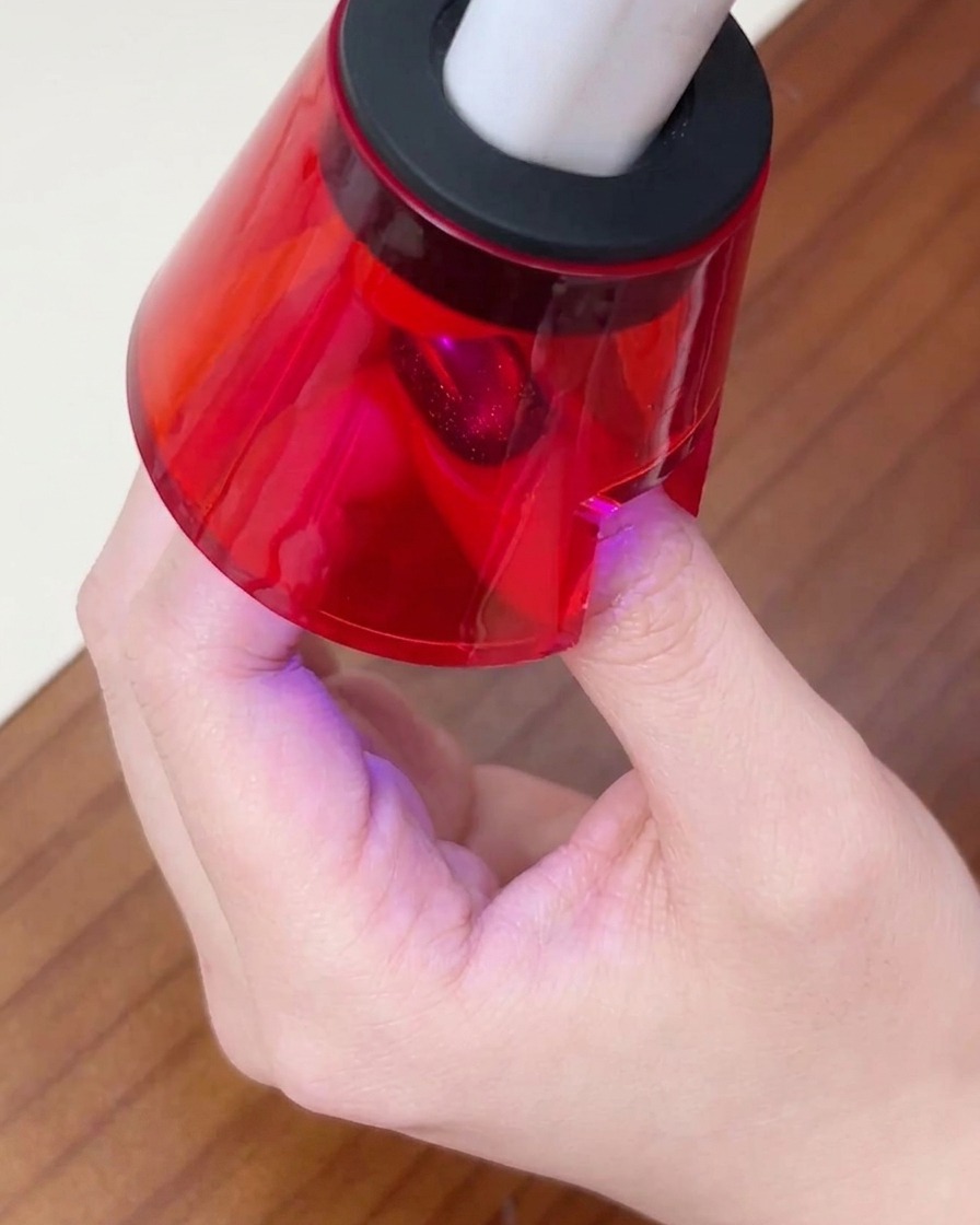 Der Finger einer Person ruht unter einer kleinen, roten UV/LED-Nagellampe, um die letzte Gelschicht auszuhärten.