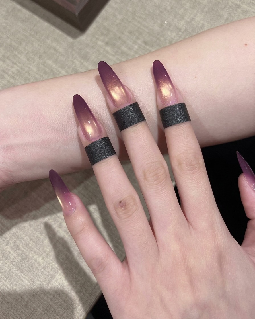 Ein Nagelpinsel trägt eine Schicht schimmerndes, goldenes Cat-Eye-Gel über den violetten Ombré-Verlauf auf.